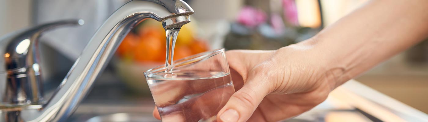 Hand holding glass under tap of running water.