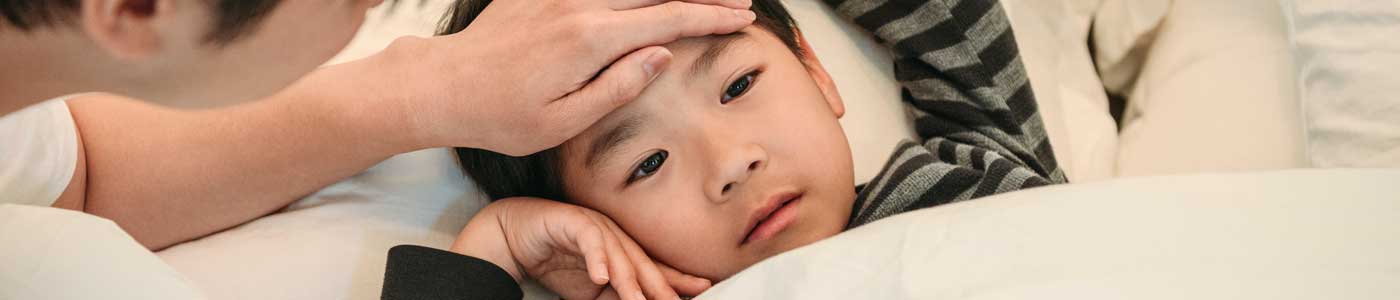 Sick child in bed with adult hand on their forehead