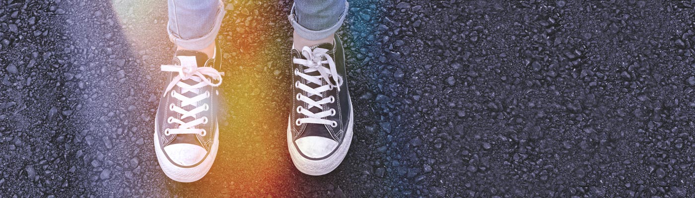 Person standing on pavement with rainbow light shining over running shoes