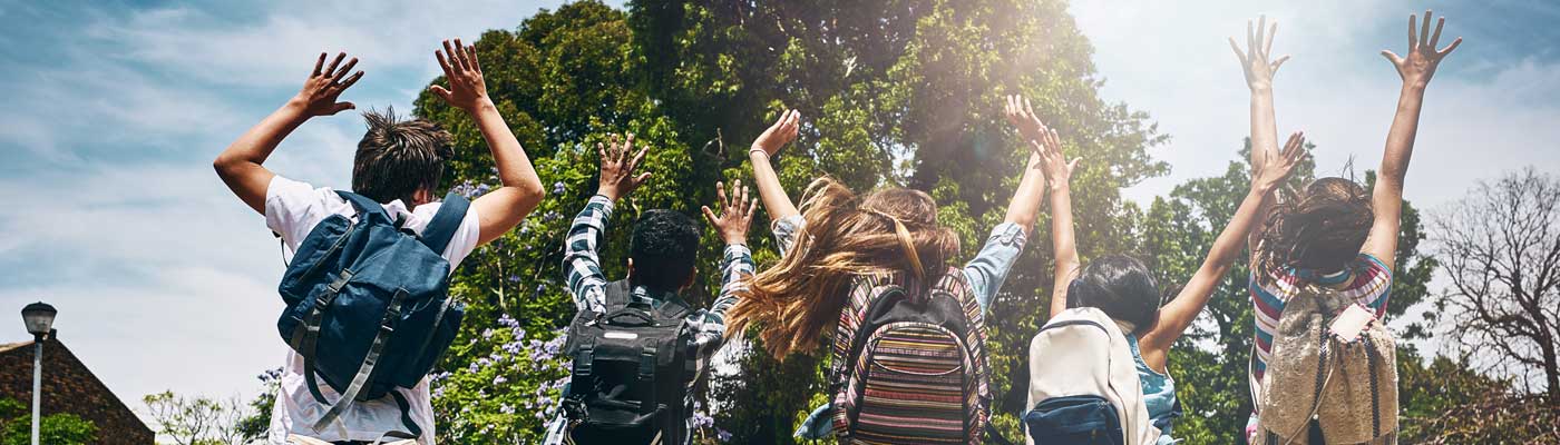 Children wearing backpacks outside jumping into the air