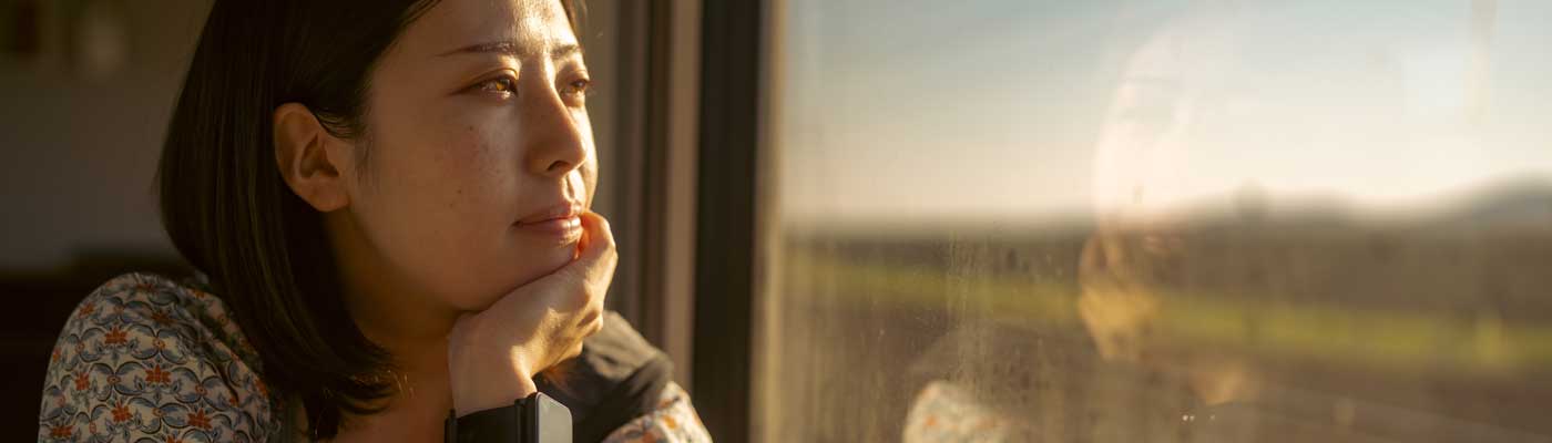 Person with a neutral expression in warm light looking out of a window
