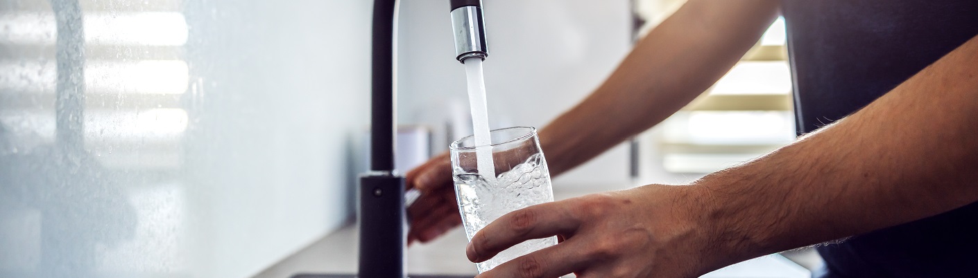 Personne versant de l'eau dans un verre du robinet de la cuisine