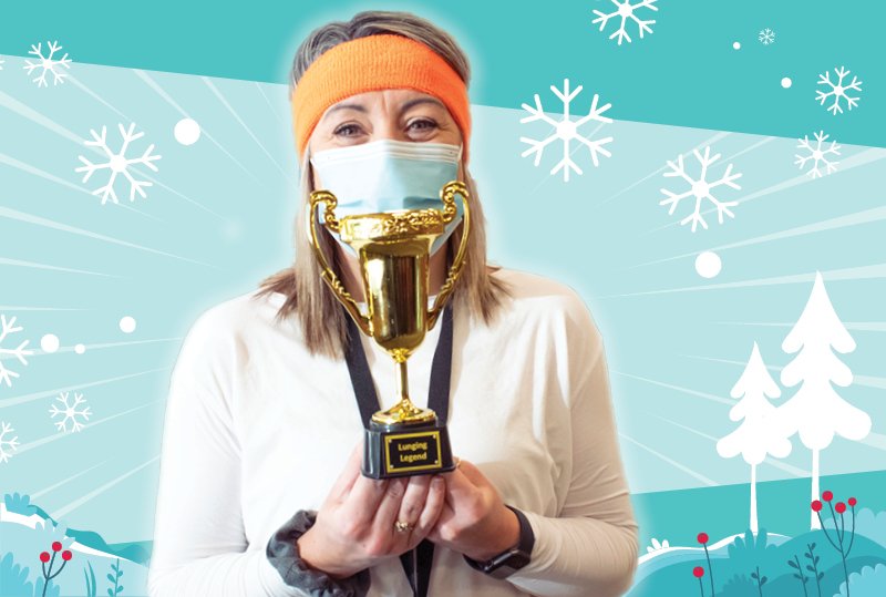 Person in mask standing against a snowy backdrop holding a trophy