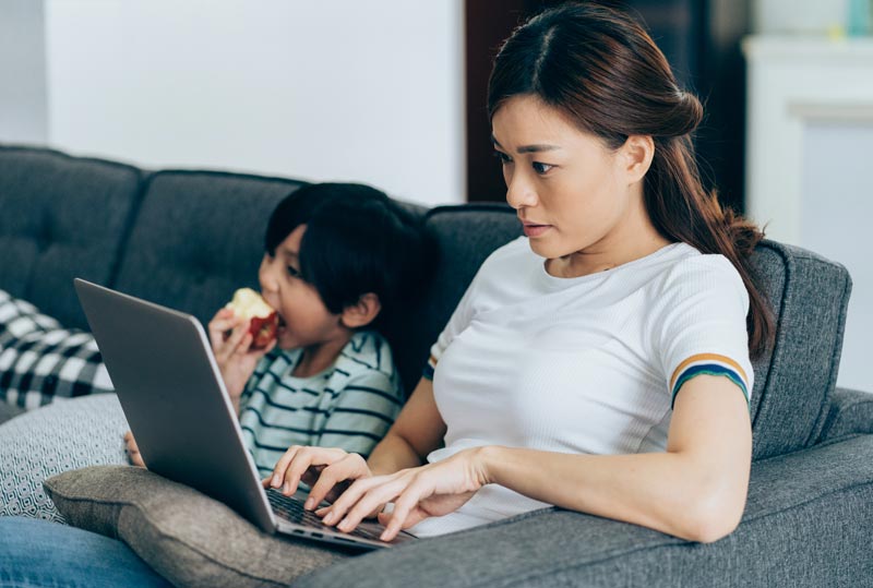 Adult on couch with laptop, child on couch with apple